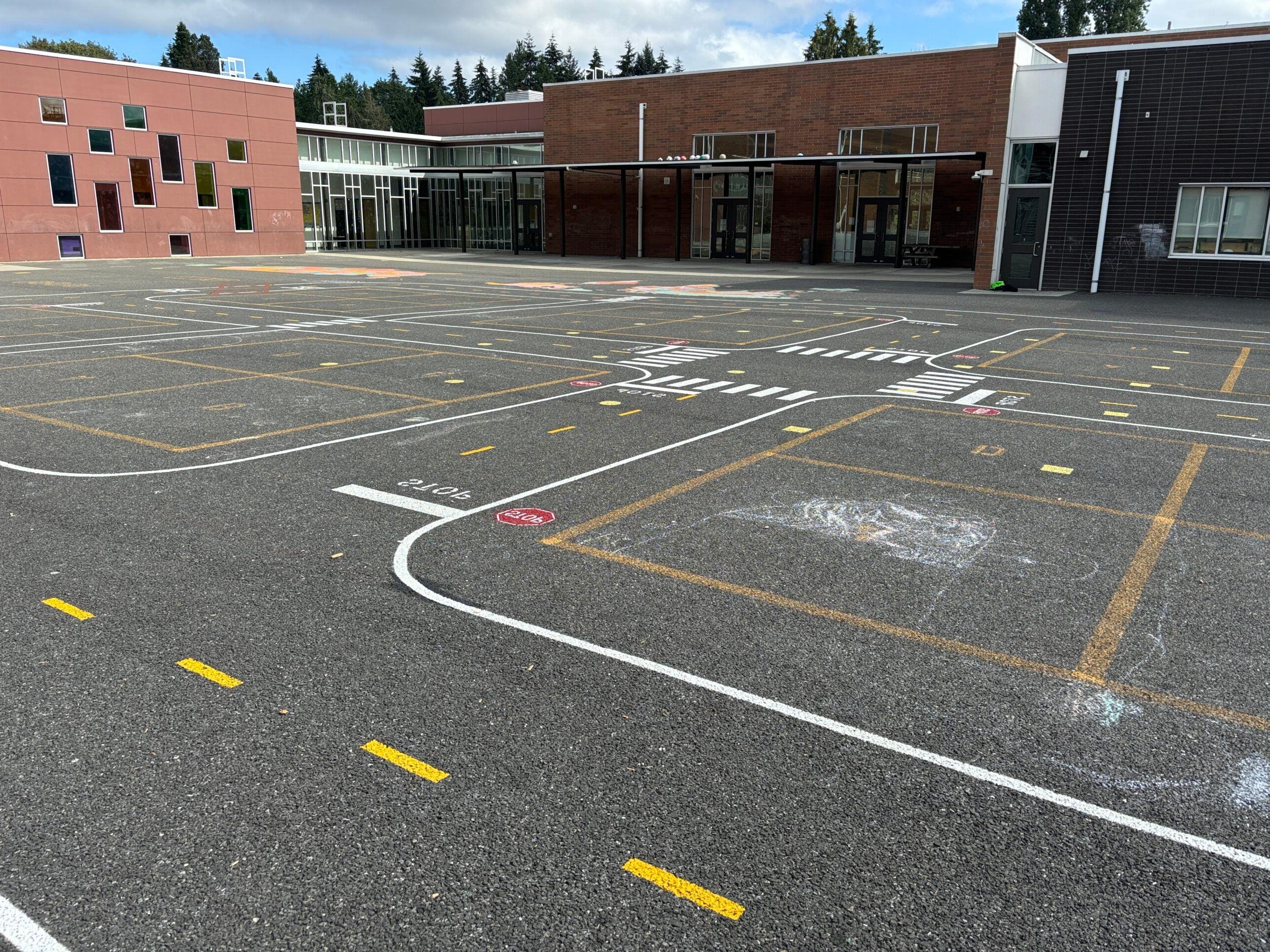 Miniature painted road curves around four square court and student chalk art. 穿着黑色上衣，背景是学校.